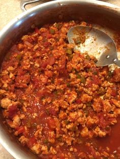 a large pot filled with meat and sauce on top of a counter next to a wooden spoon