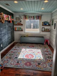 a room with a rug, window and chalkboard on the wall