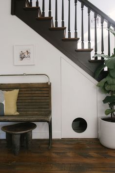 a wooden bench sitting under a stair case next to a potted plant on top of a hard wood floor