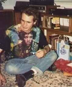 a young man sitting on the floor looking at his cell phone while holding something in his hand