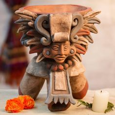 a vase with an animal head on it next to a candle and some orange flowers