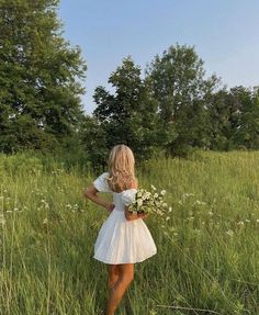 a woman in a white dress is standing in tall grass and holding a bouquet of flowers