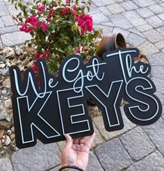 we got the keys sign in front of a potted plant with flowers behind it