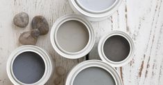 four white paint cans sitting on top of a wooden table next to rocks and pebbles