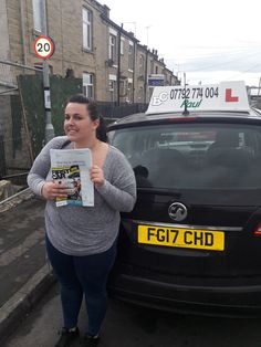 a woman standing next to a car holding a magazine