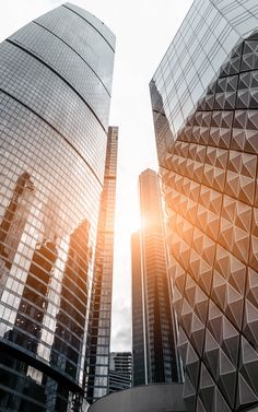 some very tall buildings near each other with the sun shining through them in the background