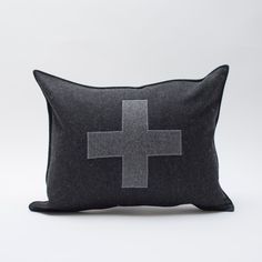 a black and grey pillow with a cross on the front, sitting against a white background