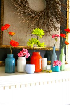 colorful vases are lined up on the mantle in front of a painting and wreath