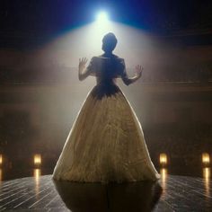 a woman in a white dress standing on a stage with her hands out to the side