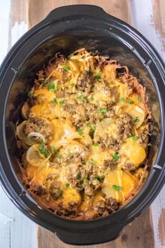 a crock pot filled with meat, potatoes and cheese on top of a wooden table