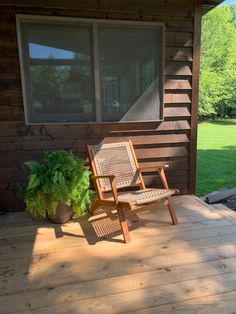 a wooden chair sitting on top of a wooden deck next to a window and potted plant