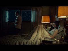 a woman laying on top of a bed in a bedroom next to a man standing