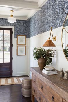 the entryway is decorated with blue and white wallpaper, an antique dresser, and a large round mirror