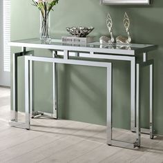 a console table with glass top and chrome legs in a green living room, decorated with flowers