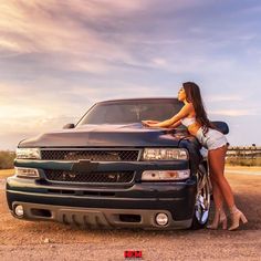 a beautiful woman leaning on the hood of a black truck with her legs up against it