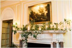 an ornate fireplace with candles and greenery in front of a painting on the wall