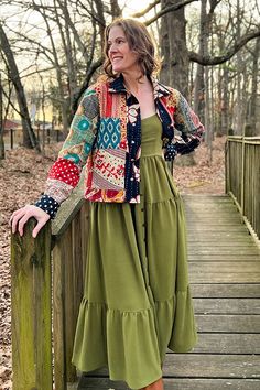 a woman standing on a wooden bridge wearing a green dress and colorful cardigan jacket