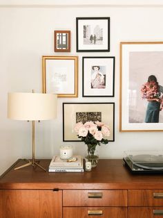 a wooden dresser topped with lots of pictures next to a lamp and a record player