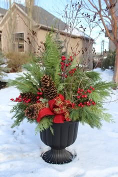 a potted plant in the snow with pine cones and red ribbon on it's top