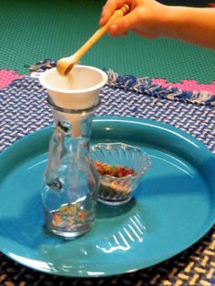 a person holding a wooden spoon over a glass bottle on a blue plate with two small bowls