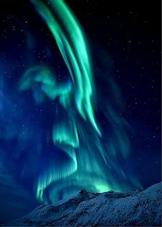 an aurora bore is seen in the night sky above some snow covered mountains and trees