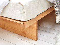 a wooden bed frame with white sheets on top of it and a rug next to it