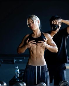 a man and woman standing next to each other in front of dumbbells with their hands on their hips