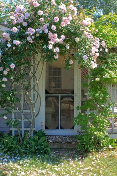 a white house with pink flowers on the front door and side window, surrounded by greenery