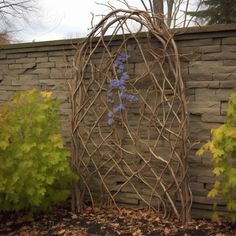 an outdoor sculpture made out of branches and twigs with blue flowers in the center, next to a brick wall