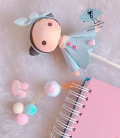 a small doll is next to a notepad, pen and keychain on a white furnishing