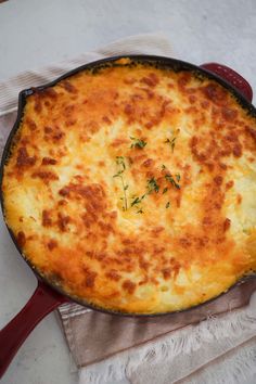 a cheesy casserole in a red cast iron skillet on a white cloth