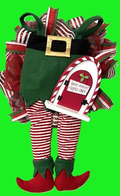 a christmas elf holding a mailbox in front of a green background with red and white striped stockings