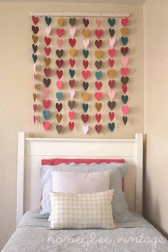 a bed topped with a white headboard covered in pillows and paper hearts hanging on the wall