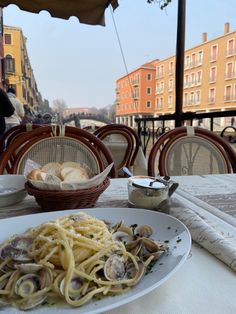 a plate of pasta with clams and bread on a table in an outdoor cafe