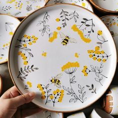 a plate with yellow flowers and bees painted on the front is surrounded by other plates