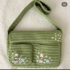 a green crocheted purse with flowers on the front and two pockets at the bottom