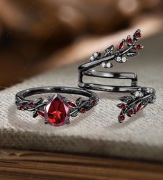 two silver rings with red stones and leaves on the sides, sitting on top of a book