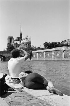 black and white photograph of two people sitting on the edge of a body of water