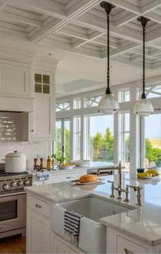 a kitchen with white cabinets and an island in front of two windows that look out onto the ocean