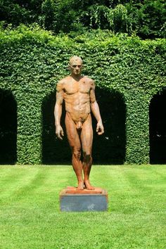 a statue of a man standing in front of a hedged area with green grass