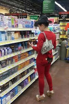 a woman in red is looking at products on the shelves inside a grocery store while holding a cell phone