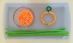 some beads are sitting in a bowl next to green and yellow sticks on a white tray