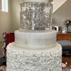 a three tiered white wedding cake with flowers on the top and bottom, sitting on a table in front of a staircase