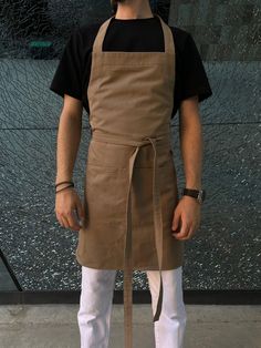 a man standing in front of a wall wearing an apron and white pants with his hands on his hips