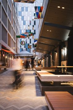 people walking and riding bicycles in an indoor shopping area with geometric tiles on the walls