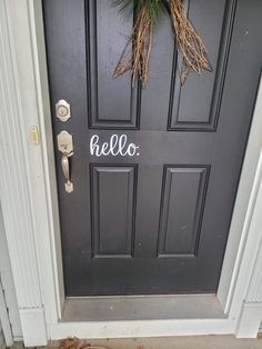 a black door with the word hello written on it and a wreath hanging from the side