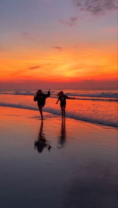 two people walking on the beach at sunset with their arms in the air as the sun sets