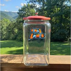 a glass jar sitting on top of a wooden table in front of a field and trees