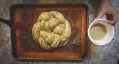 a person holding a coffee cup next to a doughnut on a baking sheet with icing