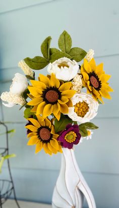 a white vase with sunflowers and other flowers in it